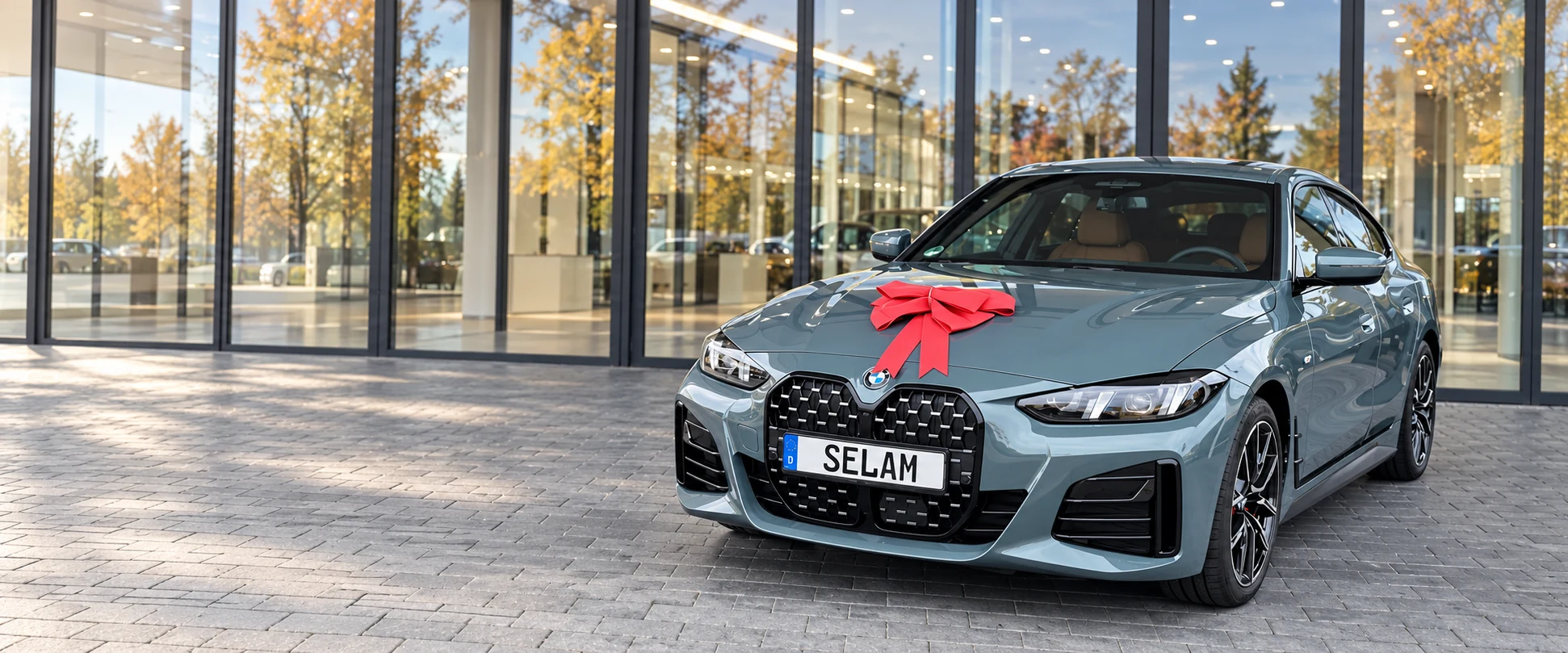 Unser BMW der 4er Reihe mit roter Schleife und SELAM-Kennzeichen vor dem gläsernen Autohaus